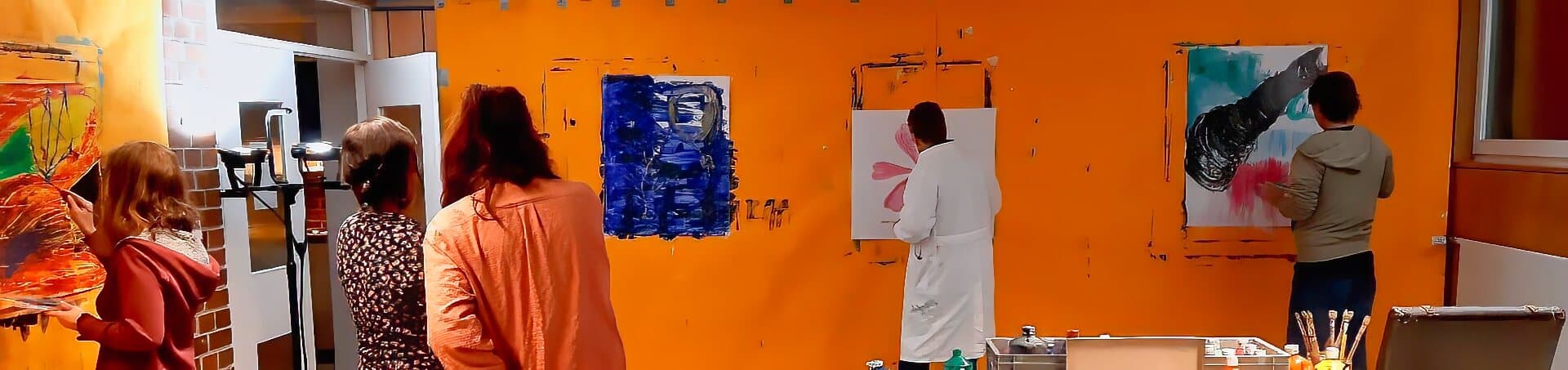 Teilnehmer eines Malkurses arbeiten an bunten Leinwänden in einem Atelier mit orangefarbener Wand.